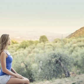 A woman in casual attire sits peacefully, enjoying a scenic outdoor view of nature.